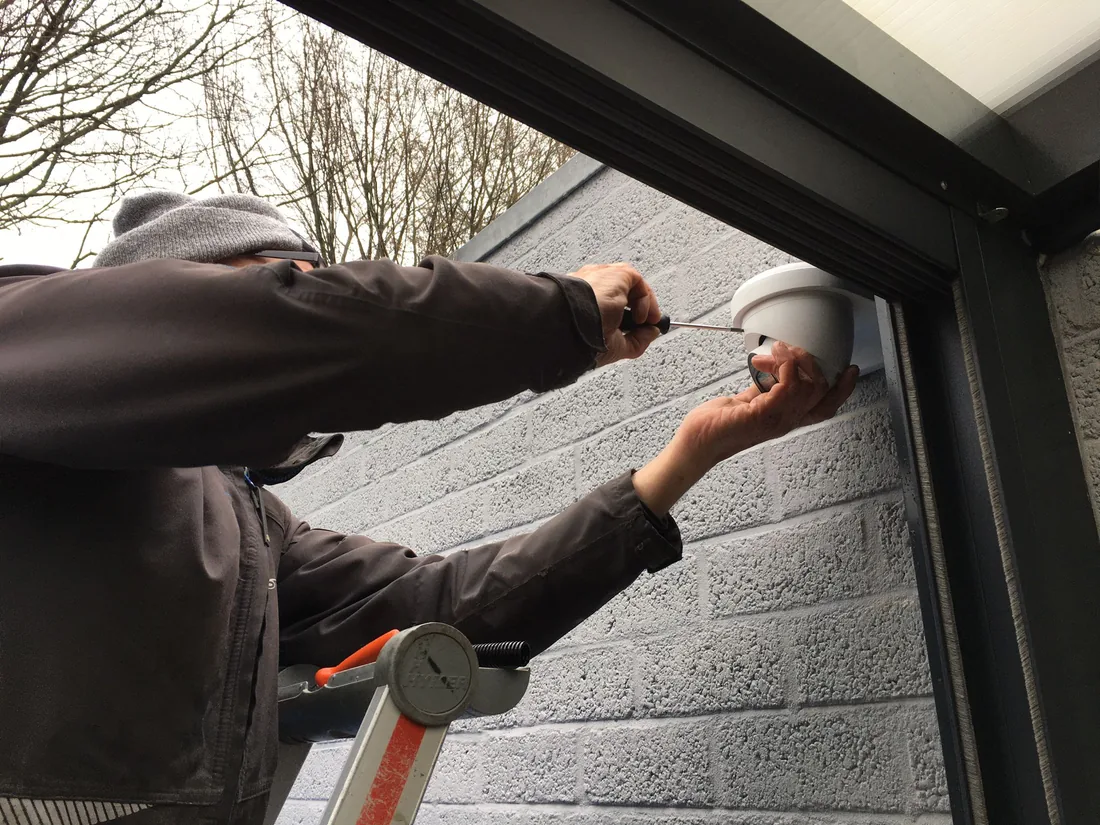 Monteur monteert een camera aan een donkere buitengevel